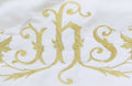 Close-up of gold embroidered IHS monogram with scrolling vines on cream canopy fabric